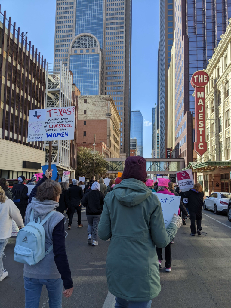 Protestors marching past The Majestic theater in Dallas. A protest sign reads, "Resist; Restore Roe; Our Bodies, Our Choice; #VOTE; Texas?! Where laws protect health [and] safety of livestock better than women"